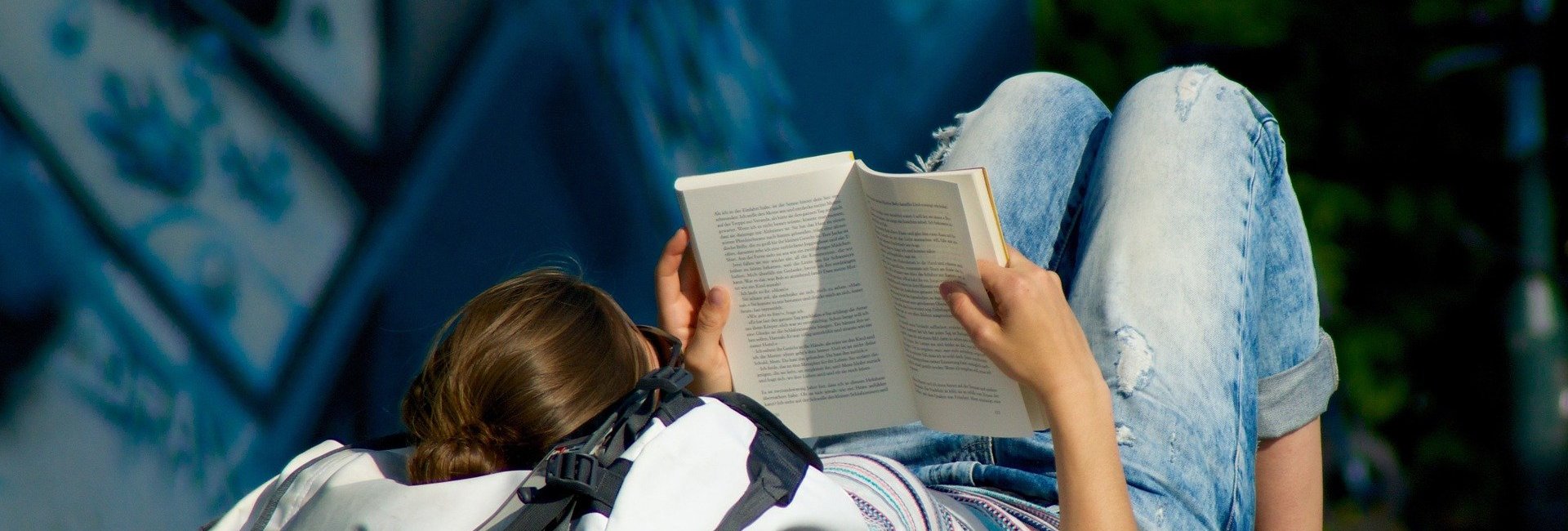 Eine junge Frau liegt in der Natur und liest ein Buch.