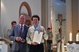 Das Bild zeigt Herrn Bürgermeister Michael Müller und Herrn Norbert Uhl. Herr Bürgermeister Müller trägt einen grauen Anzug mit grauer Krawatte und hält die Carolus-Magnus-Medaille der Gemeinde Bobenheim-Roxheim in der Hand. Herr Uhl trägt die Pfadfinderkleidung und hält die zur Carolus-Magnus-Medaille ausgehändigte Urkunde in der Hand.