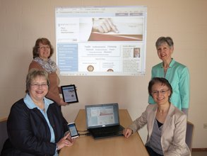 im Bild sind von links Annette Hesch, Martina Ulrich, Gemeindereferentin Barbara Sedlmeier und Eva Bodensohn zu sehen, welche die neue Internetseite präsentieren. Im Hintergrund ist die Startseite der neuen Internetseite zu sehen. Die Abgebildeten zeigen, dass die neue Internetseite auch über Tablet, Smartphone und Notebook erreichbar ist.
